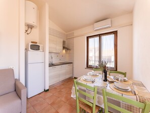 Eine kleine Küche mit Kühlschrank, Mikrowelle und Herd. Ein Esstisch mit Stühlen und ein Fenster mit Vorhängen.