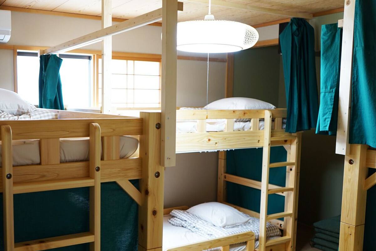 Une chambre avec un lit superposé, une fenêtre, un luminaire suspendu et une échelle en bois.