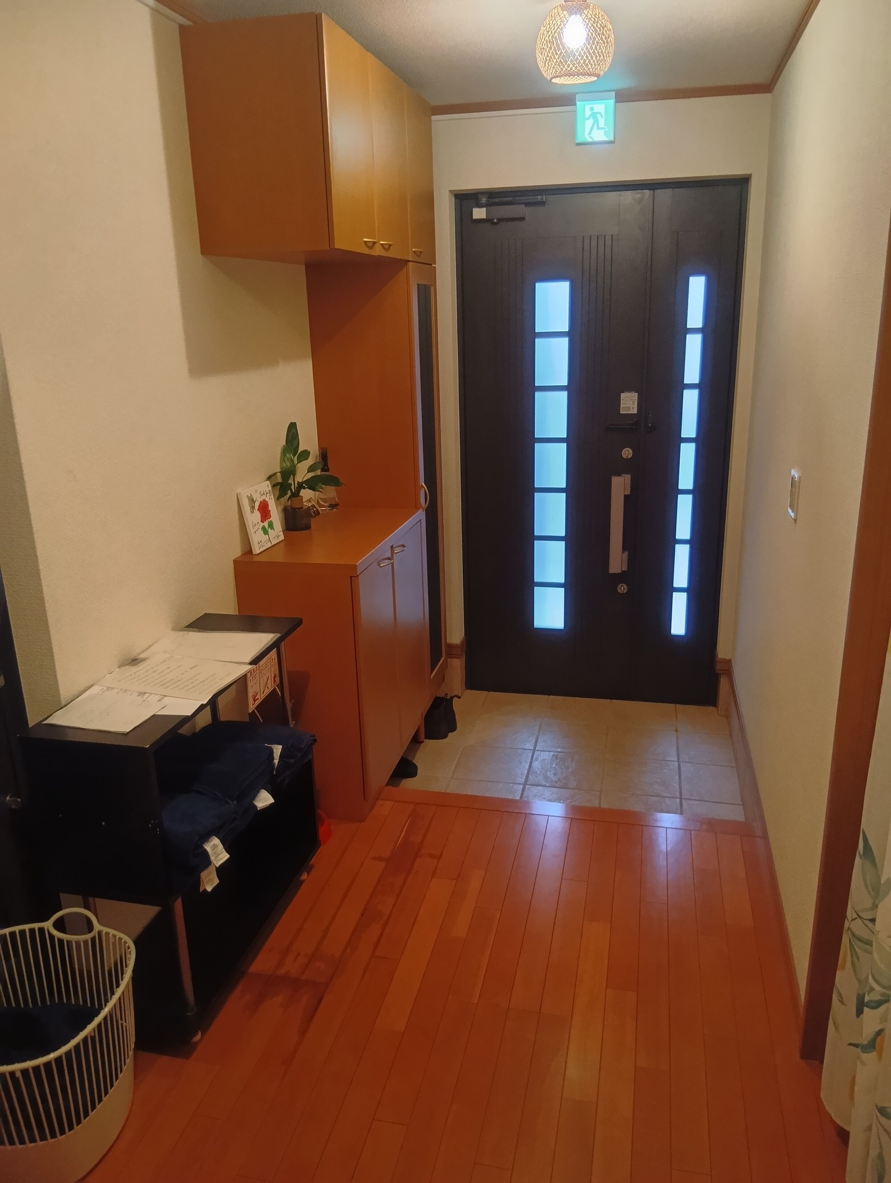 Um corredor com piso de madeira, uma escrivaninha com papéis, uma lixeira e uma porta com janela.