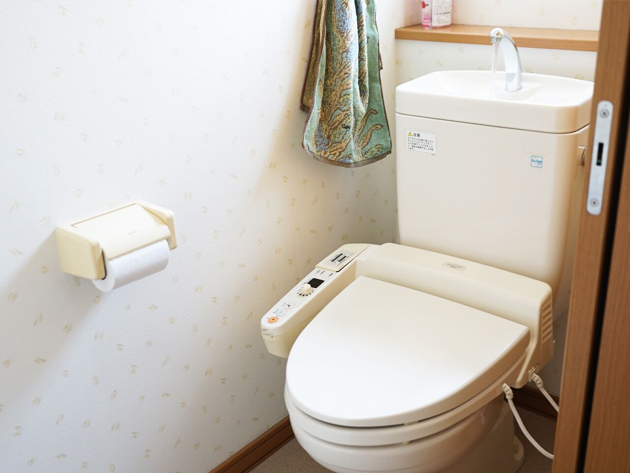 Un baño con inodoro, dispensador de toallas de papel, lavamanos y una toalla colgada en la pared.