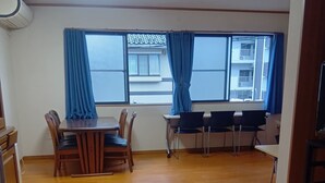 A room with a dining table, chairs, a small desk, and a window with curtains. - Eco inn - Hostel (Inazawa)