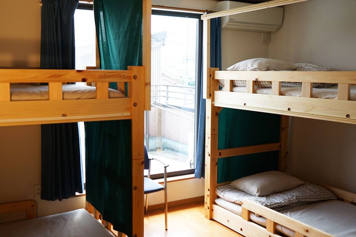 Une chambre avec un lit superposé, une fenêtre, des rideaux et une chaise.