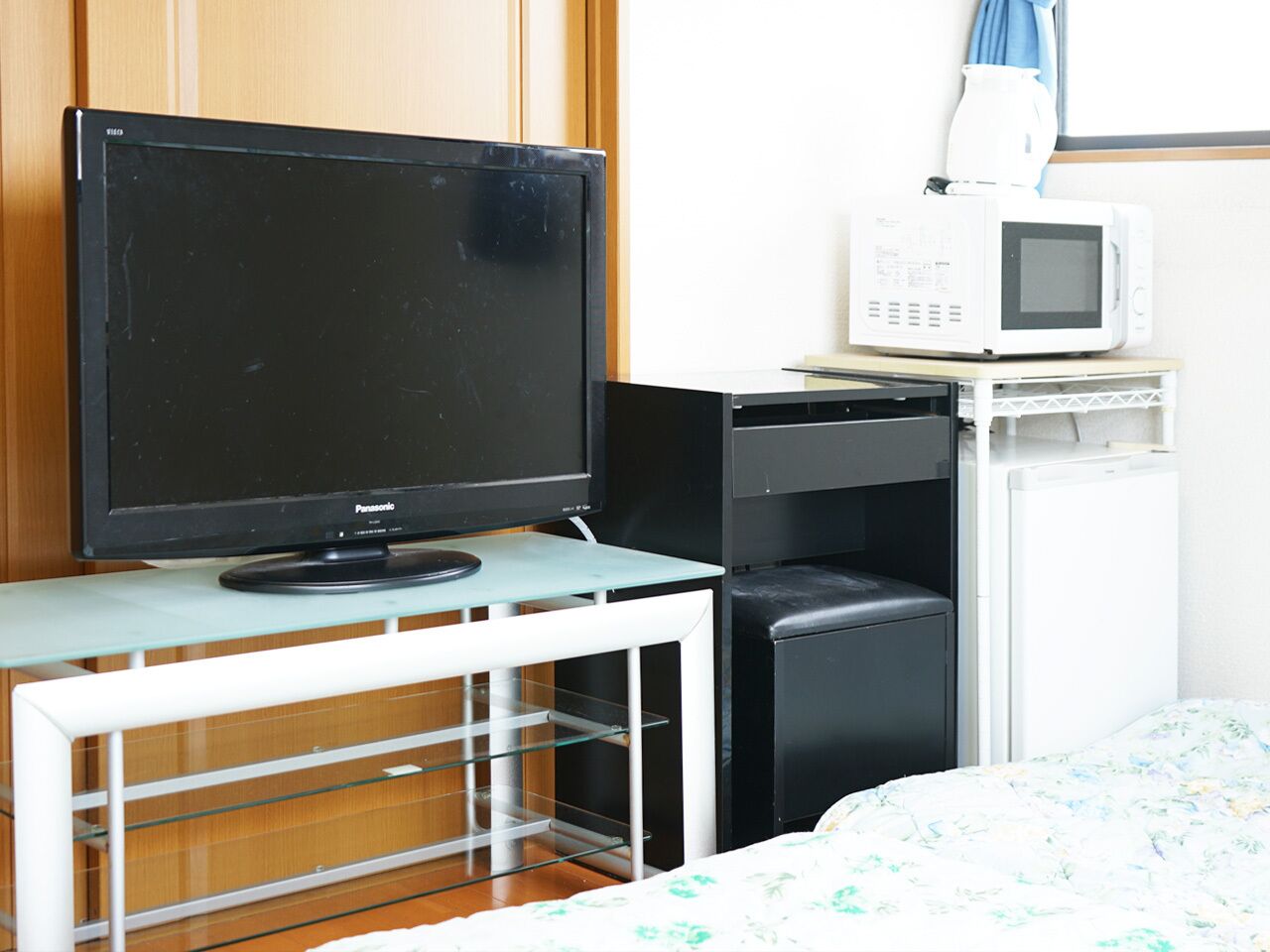 A bedroom with a television, a microwave, a small refrigerator, and a glass table.