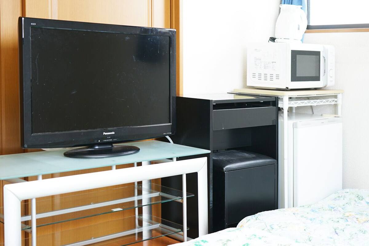 Une chambre dotée d’une télévision, d’un four à micro-ondes, d’un petit réfrigérateur et d’une table en verre.