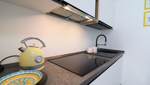 Una cocina compacta con encimera negra, un hervidor amarillo, un plato estampado y un lavamanos pequeño.