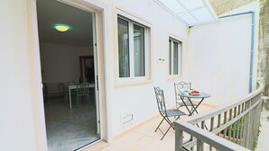 Un balcón con una mesa y sillas, una puerta que da a una habitación interior y una ventana.