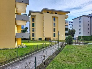 A modern apartment building with a flat roof, multiple balconies, and a well-maintained lawn with a pathway. - Lovely apartment for 4 people with WIFI, TV, balcony and panoramic view (Locarno)