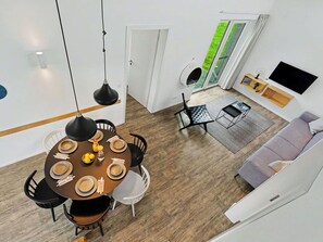Ein modernes Wohnzimmer mit Essbereich, einer Couch, einem Fernseher und Blick auf eine grüne Außenanlage.
