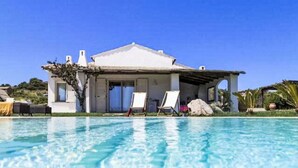 Une maison avec une piscine, un patio couvert et une façade blanche.