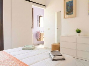 Ein Schlafzimmer mit einem Bett, einem Nachttisch mit Pflanze, einer Kommode und einem durchgegangenen Tür sichtbaren Badezimmer.