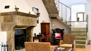Un vaste espace de vie agrémenté d’une cheminée en pierre, de meubles en osier, d’un fauteuil en cuir noir et d’un escalier menant à un niveau supérieur.