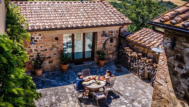 Un bâtiment en pierre avec un toit en tuiles, une terrasse avec une table ronde et des chaises, et une vue sur la campagne environnante.