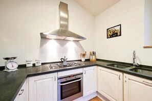 Eine Küche mit weißen Schränken, einer Edelstahl-Dunstabzugshaube, einem Gasherd, einem Backofen, einem Spülbecken und einer Waage.