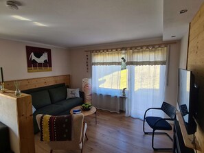 A cozy living room with a wooden floor, a green sofa, a small table with a decorative vase, and a window with sheer curtains. - "Chalet Imberg", Oberstaufen-Steibis (Oberstaufen)