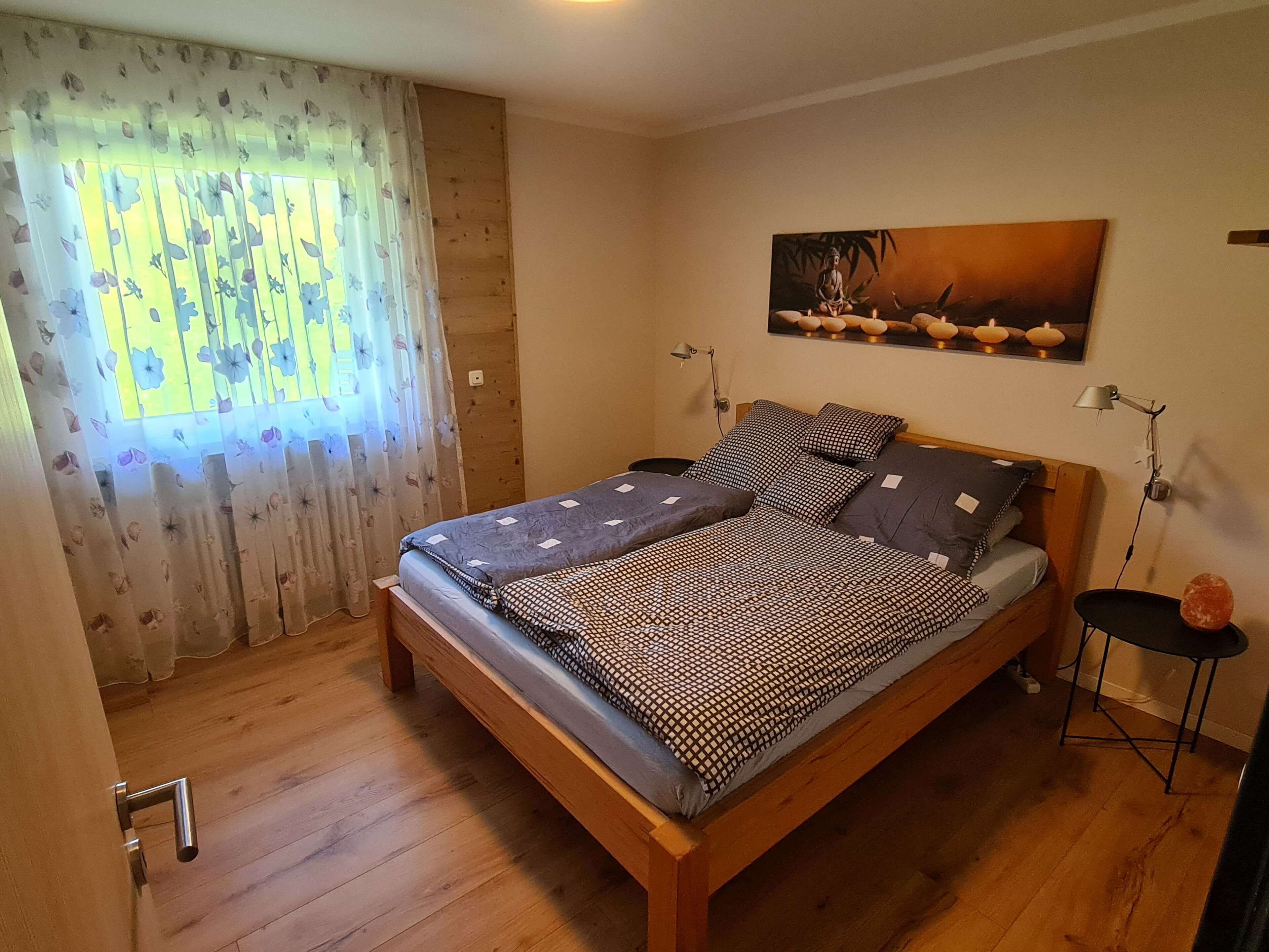 Quarto com cama de madeira, cortinas florais, pintura na parede e mesa de cabeceira com abajur.