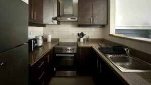 A modern kitchen with dark cabinets, stainless steel appliances, and a window providing natural light. - Silkhaus Premium 1bdr in Dubai Production City (Dubai)