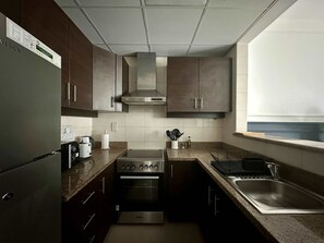 A modern kitchen with dark cabinets, stainless steel appliances, and a window providing natural light. - Silkhaus Premium 1bdr in Dubai Production City (Dubai)