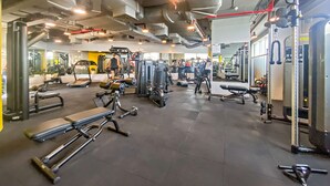 Ein Fitnessstudio mit verschiedenen Trainingsgeräten, Spiegeln und einem gefliesten Boden.