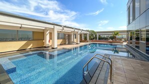 Ein moderner Hotelpoolbereich mit klarem, blauen Wasser, einer gefliesten Terrasse und Blick auf die Stadtlandschaft.