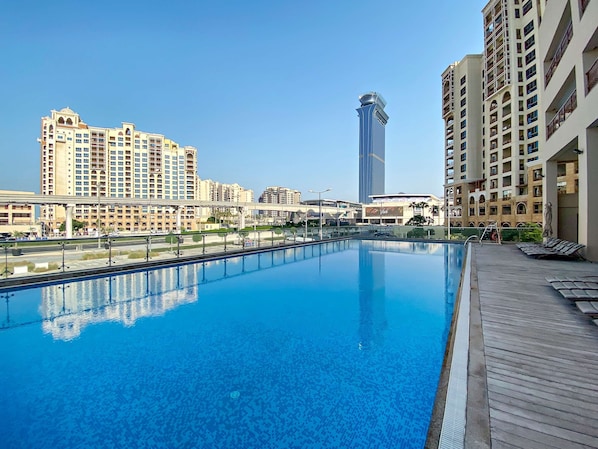 A swimming pool with a wooden deck, surrounded by high-rise buildings. - Silkhaus Seaside Studio Palm Views West Tower (Dubai)