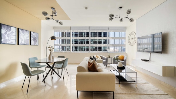 A modern living room with a dining area, large windows, a flat-screen TV, and a chandelier. - Silkhaus Luxurious 1BR Sky Gardens in Difc (Dubai)