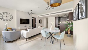 A modern living room with a sofa, a dining table with chairs, a TV, and a large clock on the wall. - Silkhaus Luxurious 1BR Sky Gardens in Difc (Dubai)