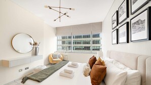 A modern bedroom with a large bed, a round mirror, a window with a view, and framed pictures on the wall. - Silkhaus Luxurious 1BR Sky Gardens in Difc (Dubai)