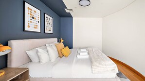 A modern bedroom with a large bed, a bedside table, a lamp, and artwork on the wall. - Silkhaus Comfy Studio in Sky Gardens Difc Views (Dubai)