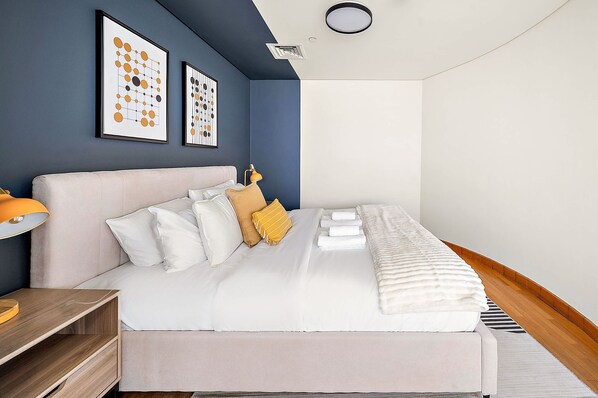 A modern bedroom with a large bed, a bedside table, a lamp, and artwork on the wall. - Silkhaus Comfy Studio in Sky Gardens Difc Views (Dubai)