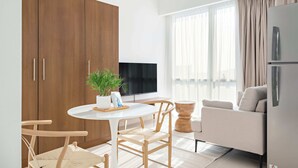 Apartamento moderno com área de refeições, sofá, televisão e uma grande janela com cortinas.