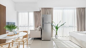 A modern, well-lit living room with a white sofa, a dining table with chairs, a refrigerator, and a potted plant. - Silkhaus Luxury Studio Nova Tower High Floor (Dubai)