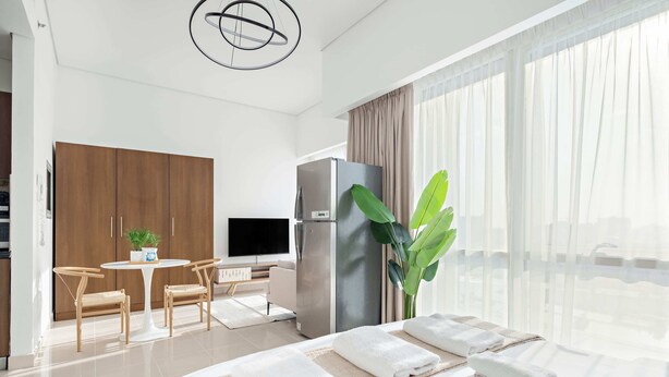A modern hotel room with a bed, a dining area, a refrigerator, and a large window with curtains. - Silkhaus Luxury Studio Nova Tower High Floor (Dubai)