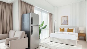 Quarto de hotel moderno com sofá, cama, geladeira, planta em vaso e pintura na parede.