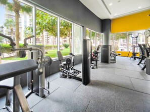 Ein Fitnessraum mit unterschiedlichen Trainingsgeräten, großen Fenstern und Blick auf eine grüne Außenanlage.