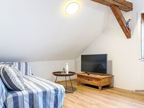 Ein gemütliches Schlafzimmer im Dachgeschoss mit schrägen Wänden, einem großen Bett mit gestreifter Bettwäsche, einem Holztischchen, einem Fernseher und einer kleinen Dekorationsfigur.
