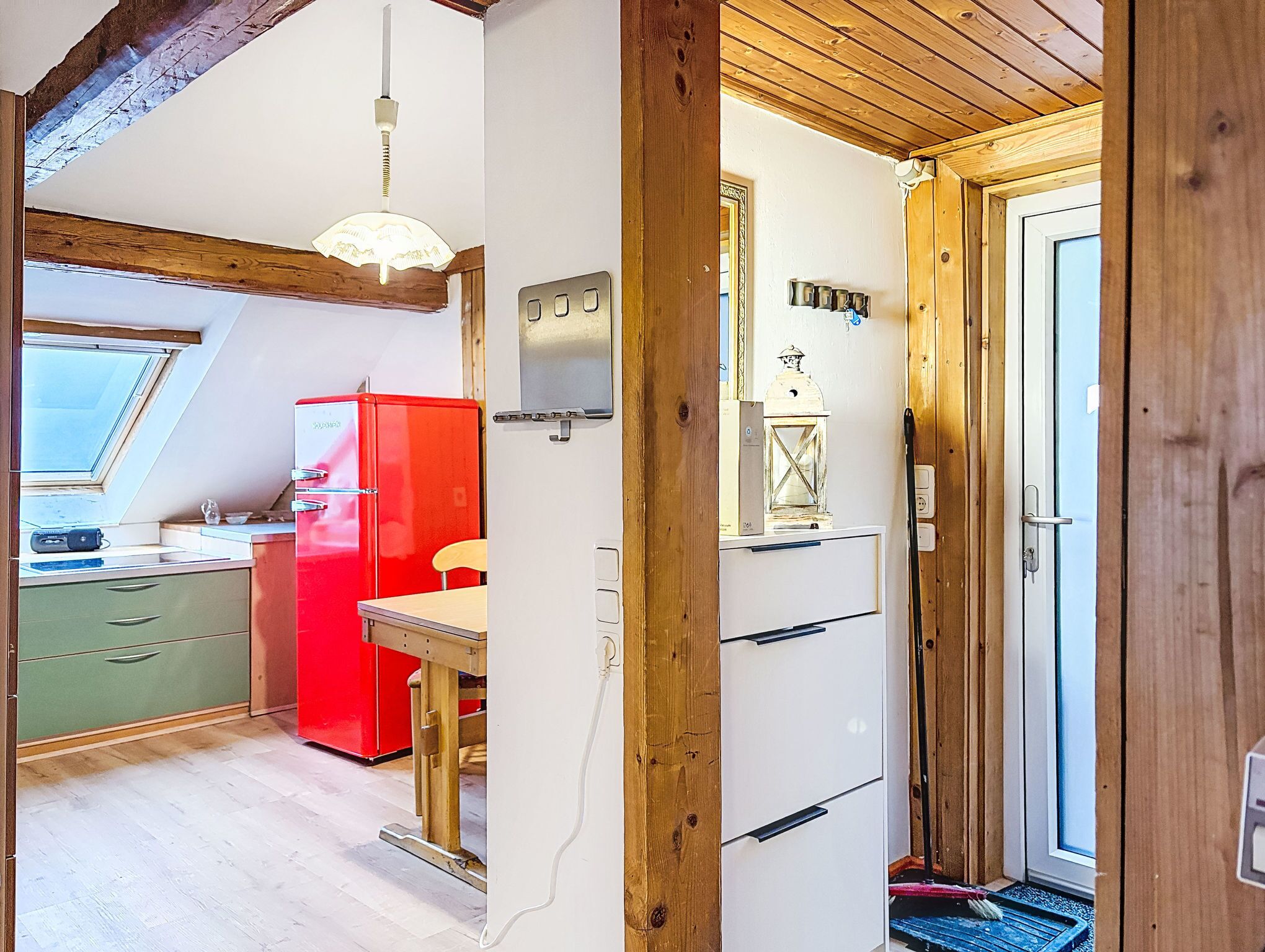 Una cocina compacta con un refrigerador rojo, una estufa blanca y techo de madera.