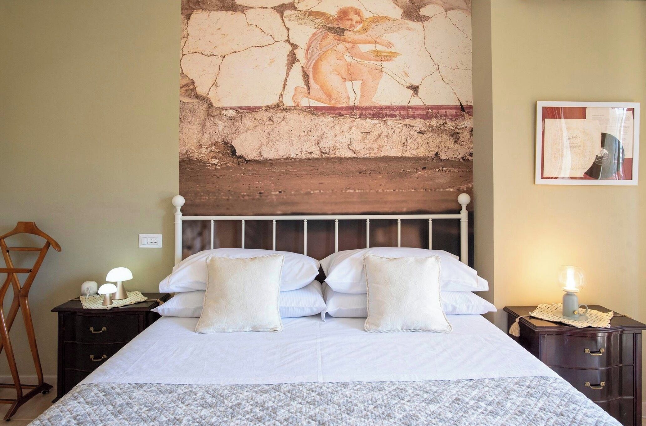 A bedroom with a bed, two bedside tables, a nightstand, a wall-mounted lamp, and a painting.