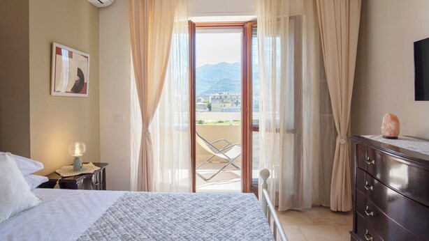 A bedroom with a bed, a bedside lamp, a dresser, a TV, and a balcony with a chair. - 3Bed-room apartment with mountain view (Castellammare di Stabia)