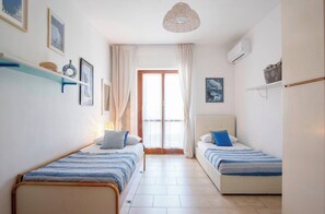 Un dormitorio con dos camas individuales, un ventanal con cortinas, un aplique colgante y un aire acondicionado instalado en la pared.