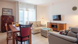 A living room with a sofa, a TV, a dining table with chairs, and a wooden cabinet. - 3Bed-room apartment with mountain view (Castellammare di Stabia)