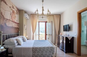 Ein Schlafzimmer mit Bett, Schminktisch, Fernseher und Meerblick durch ein Fenster.