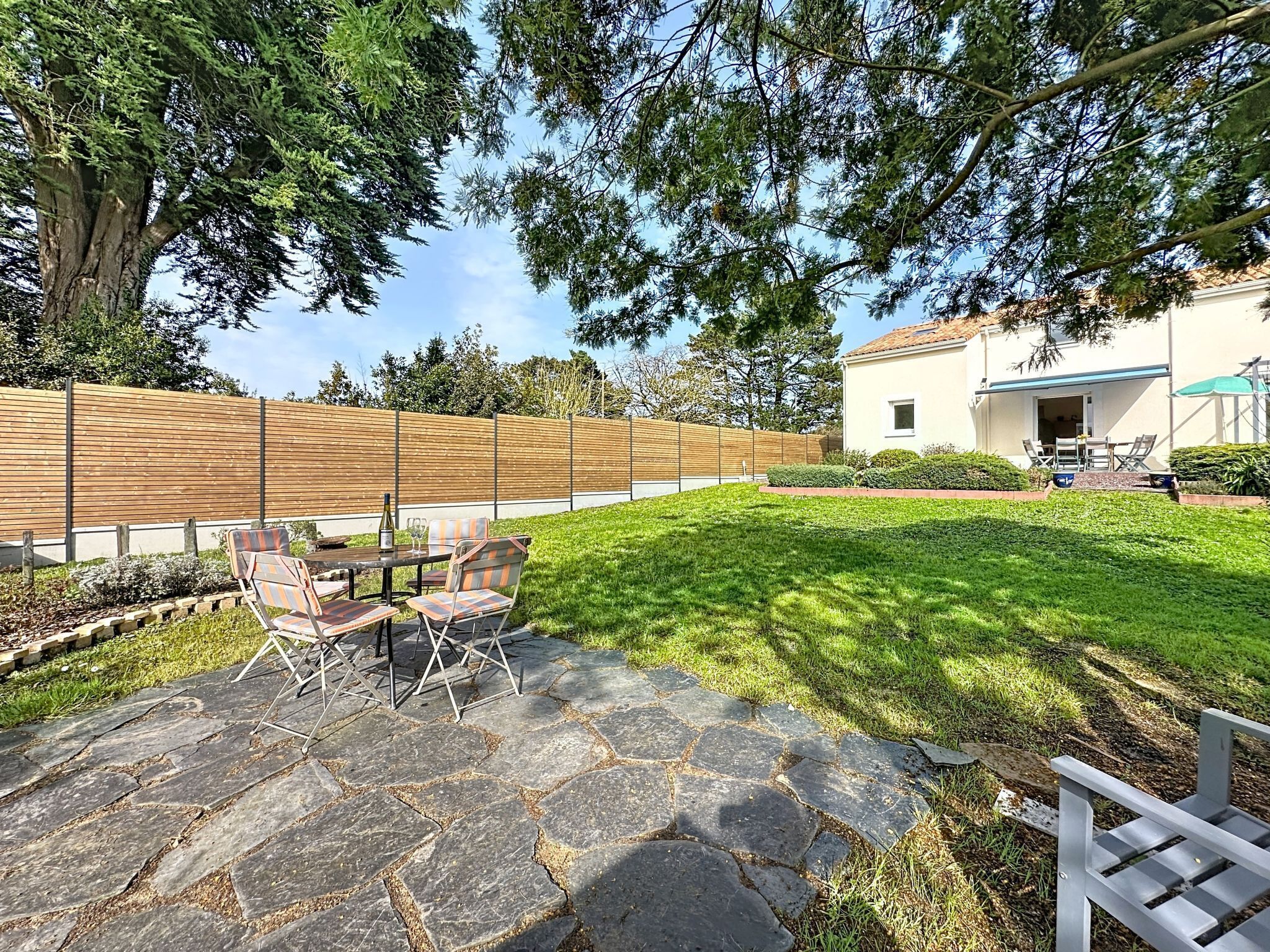 Un patio con suelo de piedra, mobiliario exterior y vista a una casa al fondo.