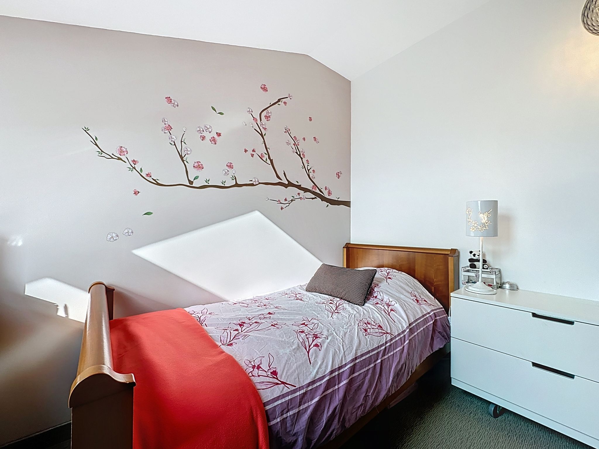 Quarto com cama, mesa de cabeceira, luminária e um objeto decorativo na parede.