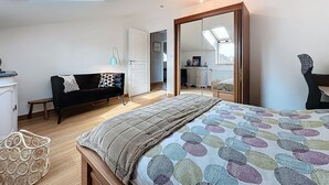 Una camera da letto con un lucernario, un letto con una coperta dai colori vivaci, un divano nero, un armadio in legno e un grande specchio.
