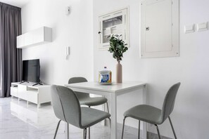 A modern living room with a white TV stand, grey chairs, a white table, and a potted plant. - Silkhaus Chic 1bdr in Oasis Tower Masdar City (Abu Dhabi)
