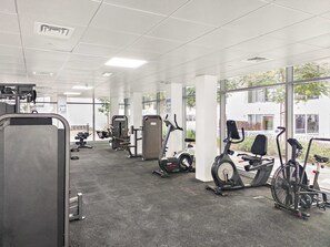 A gym with various exercise machines, large windows, and a view of the outside. - Silkhaus Chic 1bdr in Oasis Tower Masdar City (Abu Dhabi)