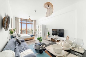 A modern living room with a sofa, coffee table, and dining area with white plates and glasses. - Silkhaus Sea View Studio in Palm Jumeirah (Dubai)