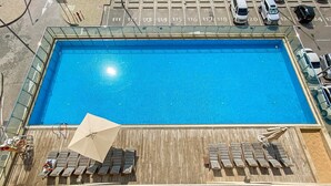 Ein rechteckiger Pool mit einer Holzterrasse, ausgestattet mit Liegestühlen und Sonnenschirmen.