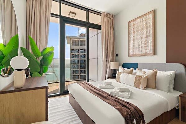 A hotel room with a large bed, a desk with a lamp, a view of a building through a sliding door, and a potted plant. - Silkhaus City View 1bdr In Maryah Vista Tower (Abu Dhabi)
