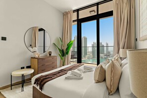 A modern hotel room with a large bed, a round mirror, a dresser, a chair, and a view of the city skyline. - Silkhaus City View 1bdr In Maryah Vista Tower (Abu Dhabi)